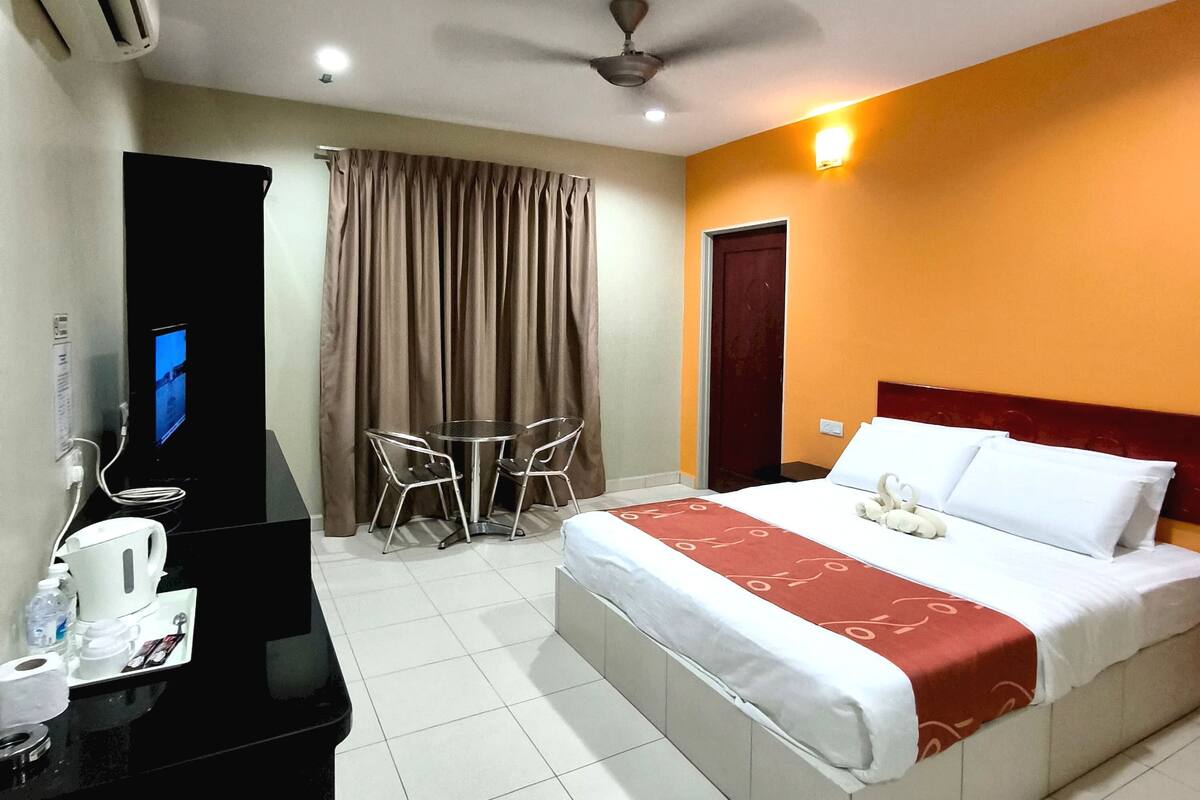 Ein Hotelzimmer mit Bett, Schreibtisch mit Computer, Stuhl, Tisch und Deckenventilator.