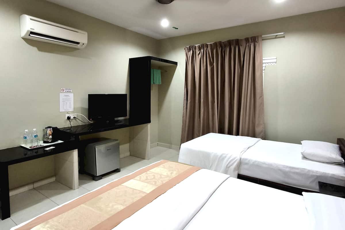 Ein Hotelzimmer mit zwei Betten, einem Schreibtisch mit Computer, einer kleinen Kühlbox, einer Klimaanlage und einem Fenster mit Vorhängen.
