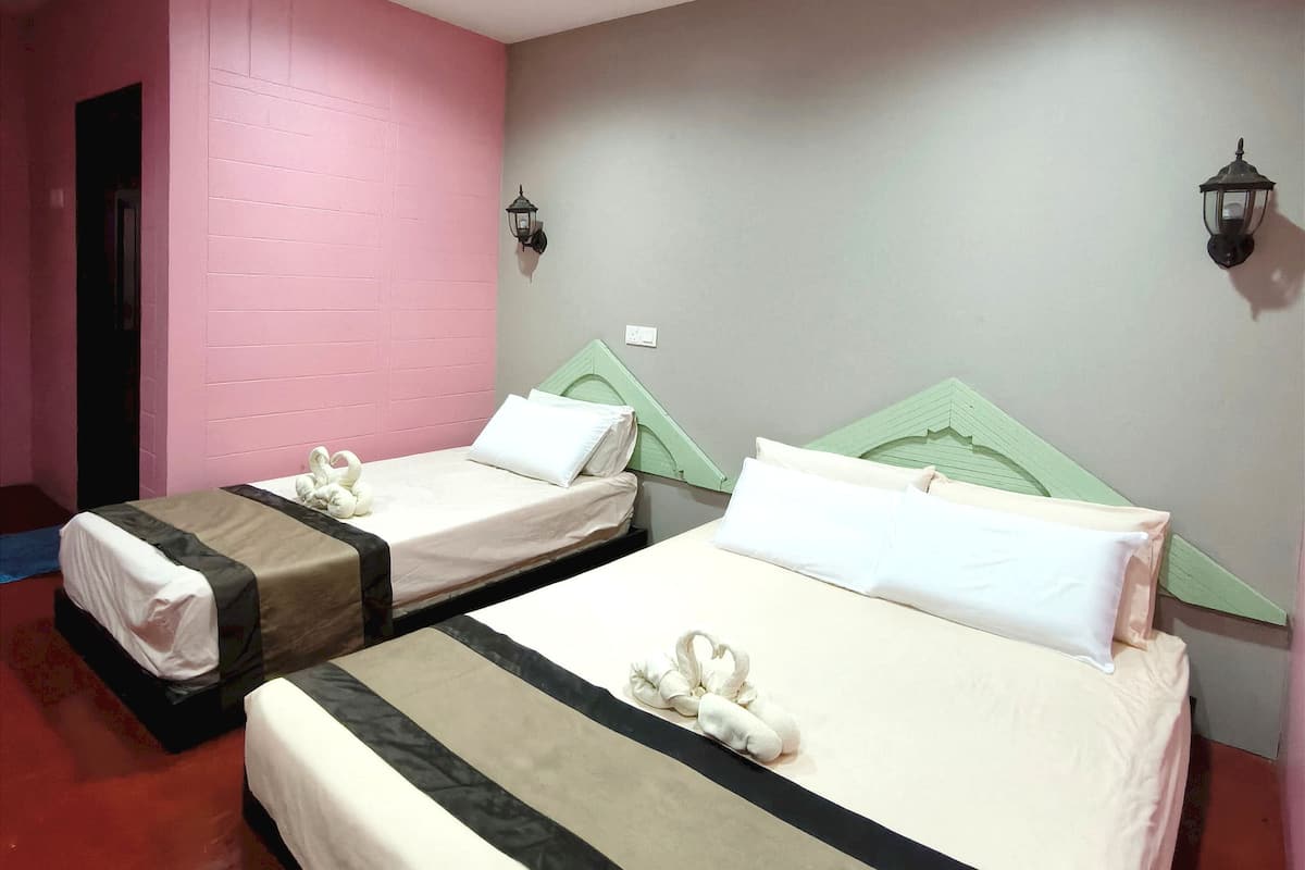 Ein Hotelzimmer mit zwei Betten, jeweils mit Kopfteil, einer Wandleuchte und einer Tür zur linken Seite.