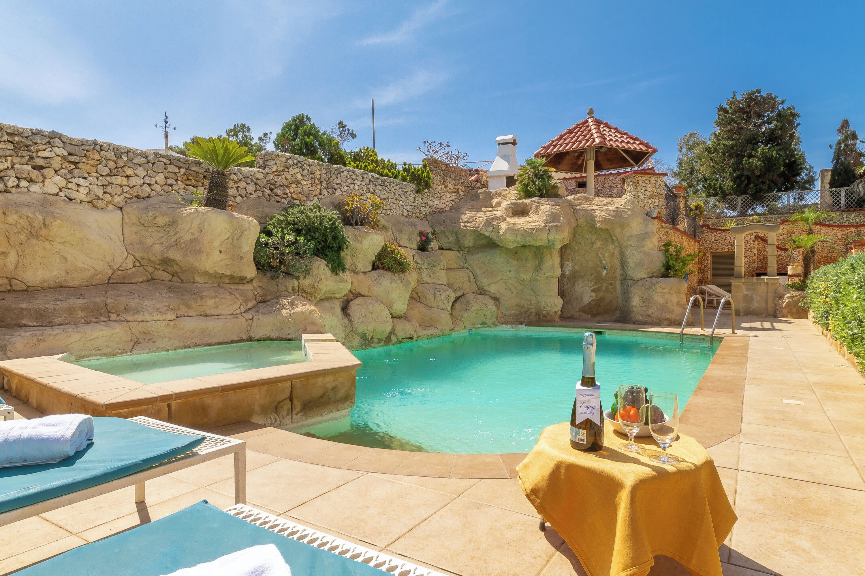 A pool area with lounge chairs and a table set with a bottle and glasses.