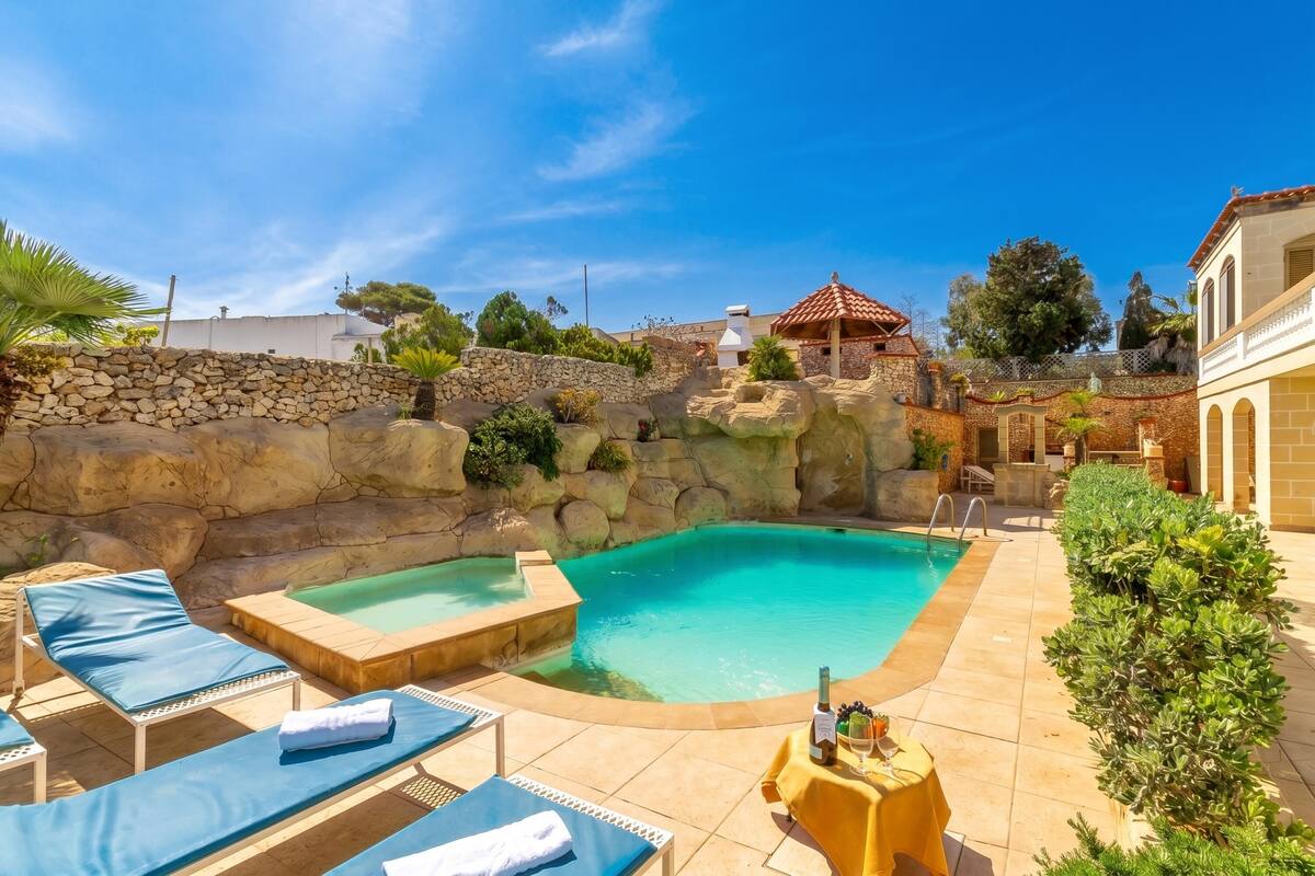 Un espace piscine avec des chaises longues, un jacuzzi et un mur en pierre.