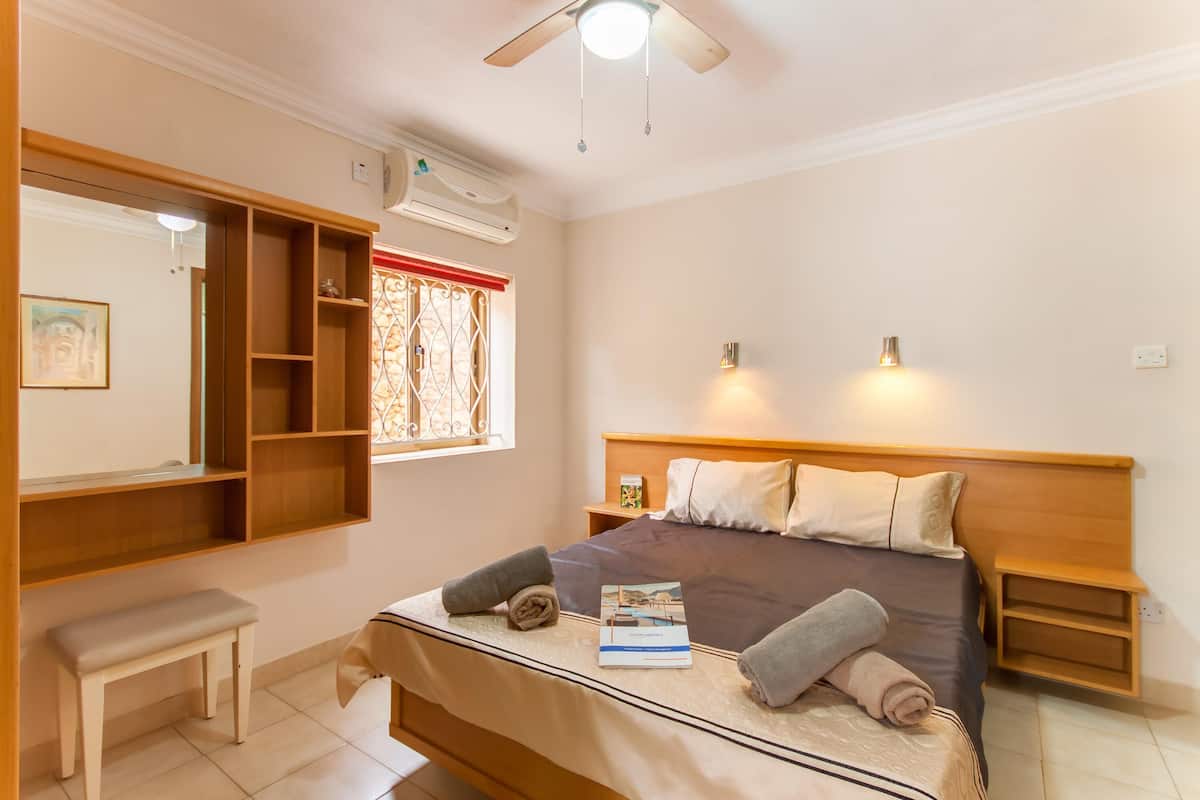 Une chambre à coucher bien aménagée, avec un lit, des tables de chevet, un banc et une fenêtre ornée de barreaux décoratifs.