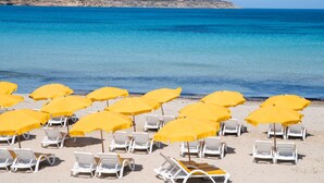 A beach with rows of white lounge chairs and yellow umbrellas. - Villa & Pool Apart in Mellieha Bay Apartments (Mellieha)