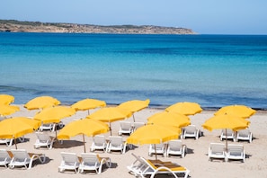 A beach with rows of white lounge chairs and yellow umbrellas.