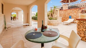 A patio with a table set for two, a bottle of wine, and a bowl of fruit. - Villa & Pool Apart in Mellieha Bay Apartments (Mellieha)