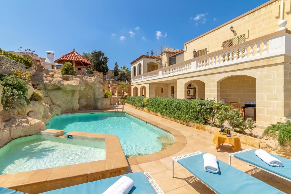 Un espace piscine doté de chaises longues et d’un jacuzzi, entouré de murs en pierre et de verdure.