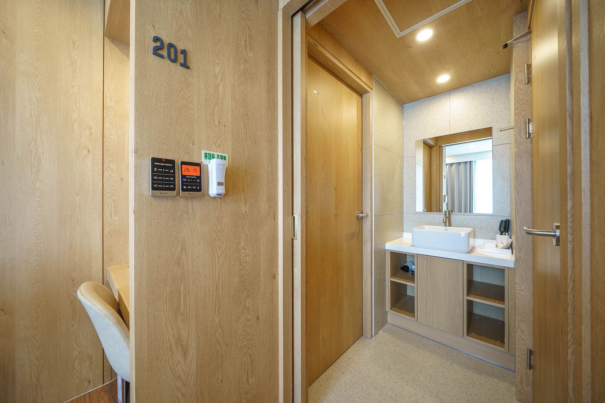 A modern bathroom with a wooden vanity, a sink, and a mirror. There are two hand sanitizer dispensers on the wall.