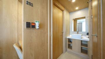 A modern bathroom with a wooden vanity, a sink, and a mirror. There are two hand sanitizer dispensers on the wall.