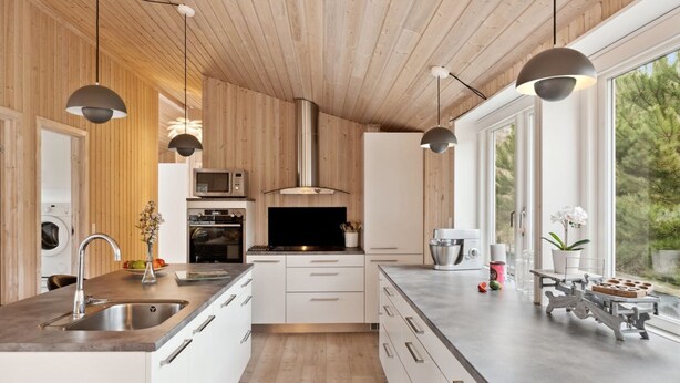 Eine moderne Küche mit Holzwänden, weißen Schränken und einem großen Fenster mit Blick auf Bäume.