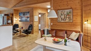 L’intérieur chaleureux d’un chalet avec des murs en bois, une table à manger ornée de fruits et de boissons, des sièges en cuir et des œuvres d’art accrochées aux murs.
