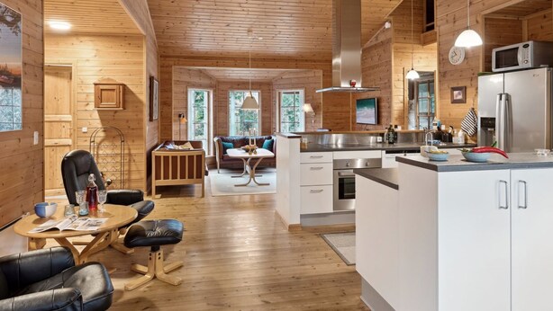 Un intérieur de chalet moderne, avec un revêtement en bois, un coin repas, une cuisine et un salon.