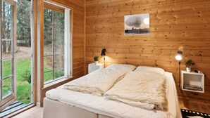 Une chambre confortable avec un plafond en bois, un grand lit, des tables de chevet avec des lampes et une vue sur l’extérieur grâce à de grandes fenêtres.