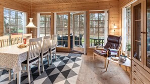 L’intérieur d’un chalet en bois comprend un coin repas, un fauteuil confortable et de grandes fenêtres.