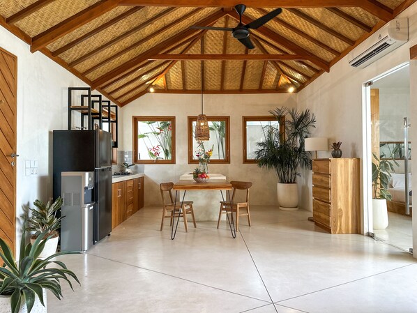 Une cuisine moderne avec des poutres en bois, un coin repas avec deux chaises, un réfrigérateur et un distributeur d’eau.