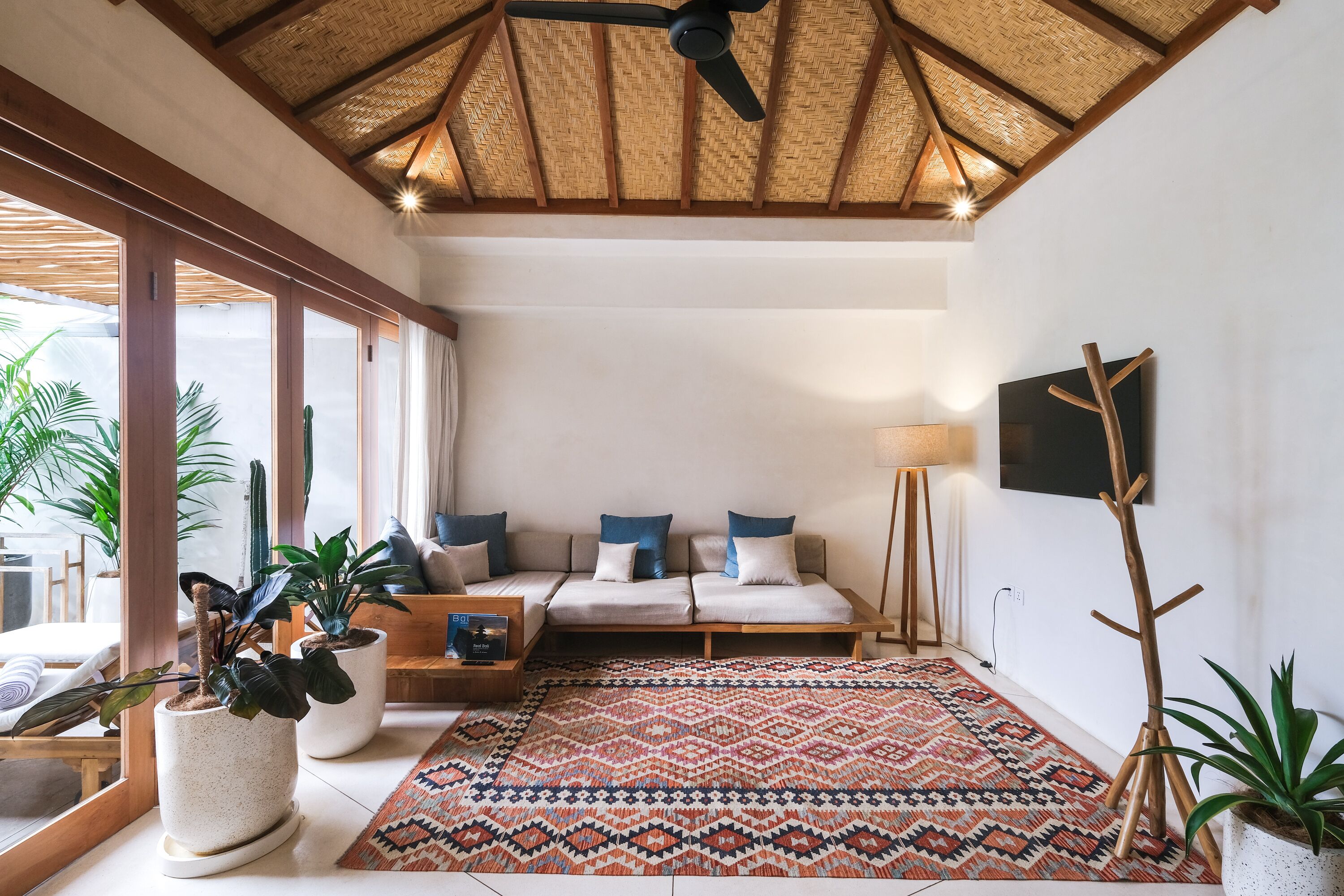 Un salon spacieux avec un grand canapé, un tapis à motifs et plusieurs plantes en pot.
