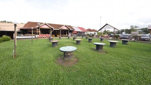 A grassy outdoor area with several round tables and a few buildings in the background. - Hotel O Noor Arfa River Chalet (Kuala Terengganu)