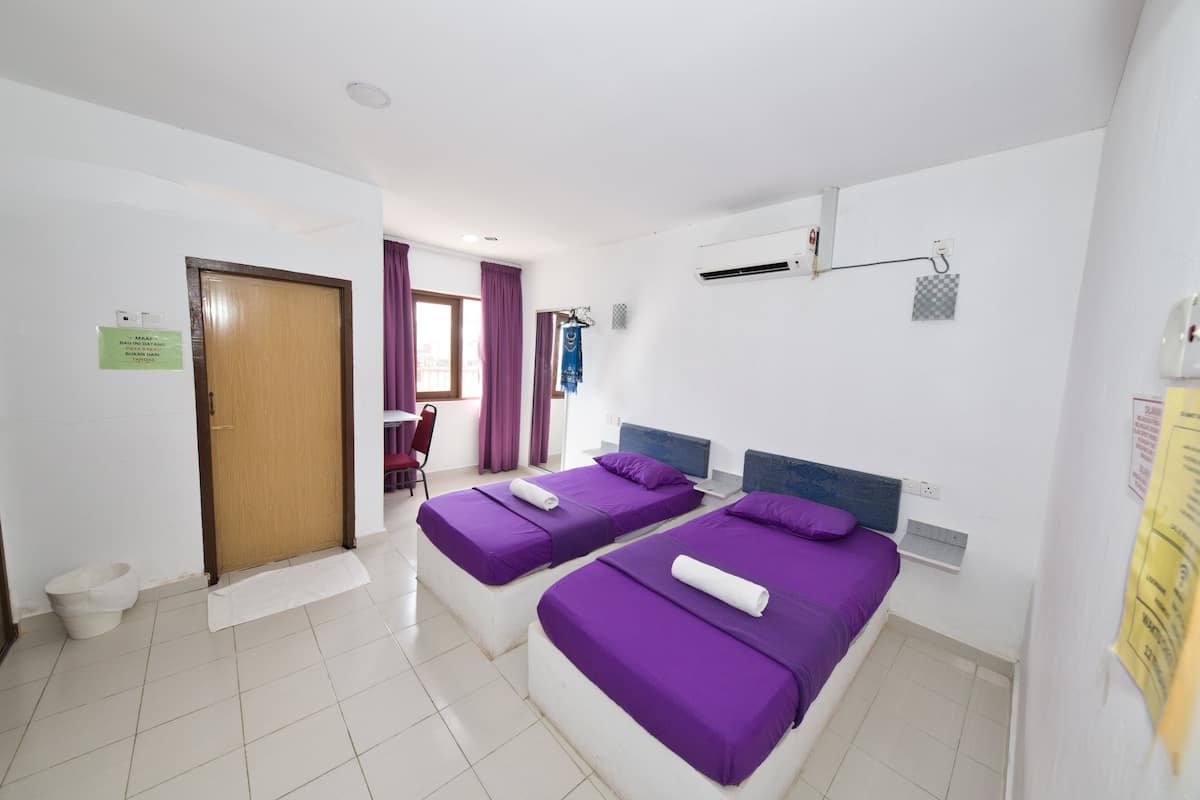 Ein Hotelzimmer mit zwei Betten, einer Holztür, einer weißen Toilette und einem Fenster mit violetten Vorhängen.