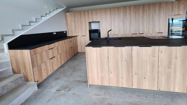 A modern kitchen with wooden cabinetry, a black countertop, and a built-in stove.