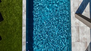 A rectangular swimming pool with clear blue water, surrounded by a stone deck and a wooden deck.