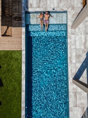 A rectangular swimming pool with clear blue water, surrounded by a stone deck and a wooden deck.