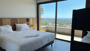 A bedroom with a bed, a bedside table, a wall-mounted light, and a view of the outdoors.