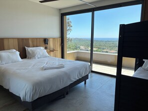 A bedroom with a bed, a bedside table, a wall-mounted light, and a view of the outdoors.
