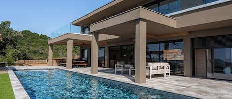 A modern house with a swimming pool, outdoor seating, and a covered patio area.