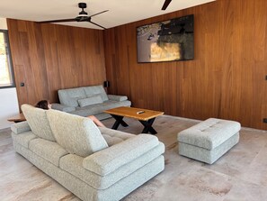 Uma sala de estar moderna com um sofá cinza, uma mesa de centro de madeira e um banquinho combinando.