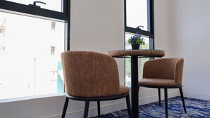 Two brown chairs with black legs around a small glass table, a potted plant on the table, and a view of buildings through large windows. - Al-Mousafer Hotel Riyadh (Riyadh)