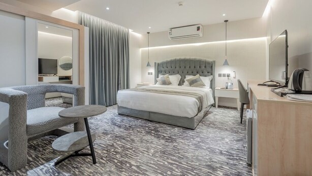 A modern hotel room with a bed, a desk, a chair, a small table, and a large mirror. - Al-Mousafer Hotel Riyadh (Riyadh)