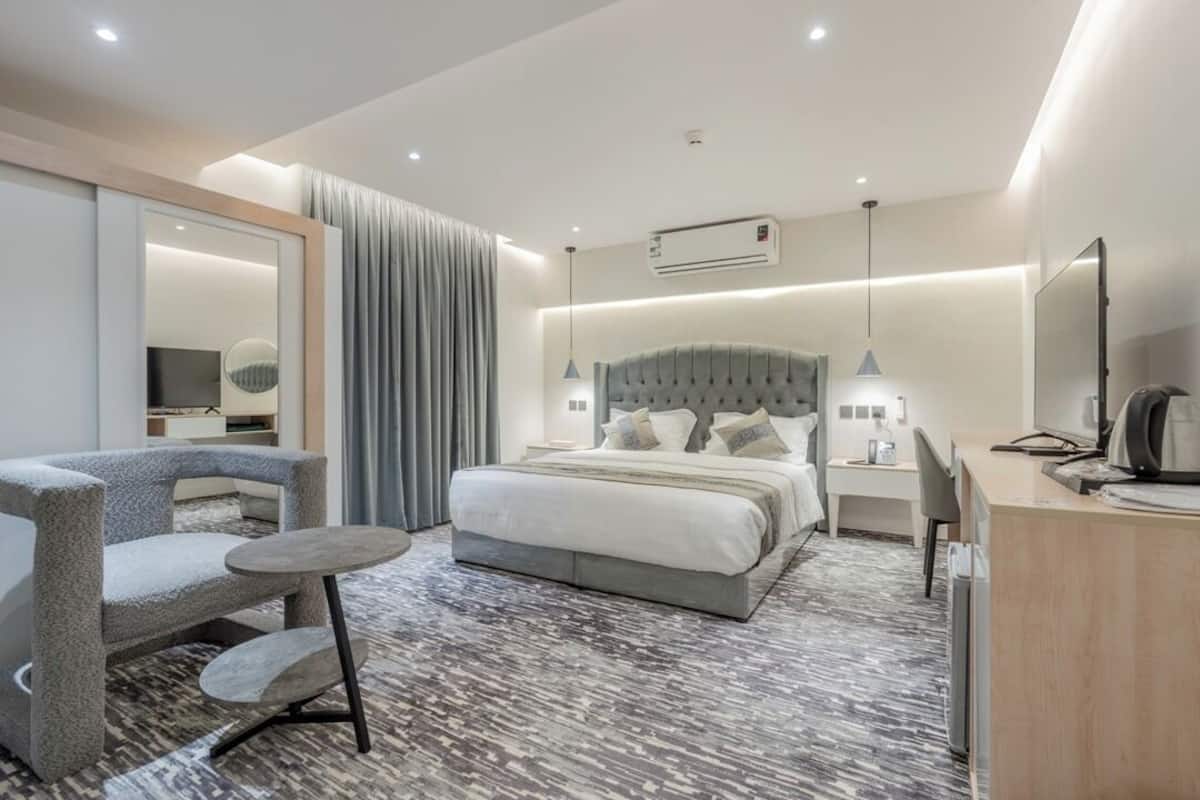 A modern hotel room with a bed, a desk, a chair, a small table, and a large mirror.