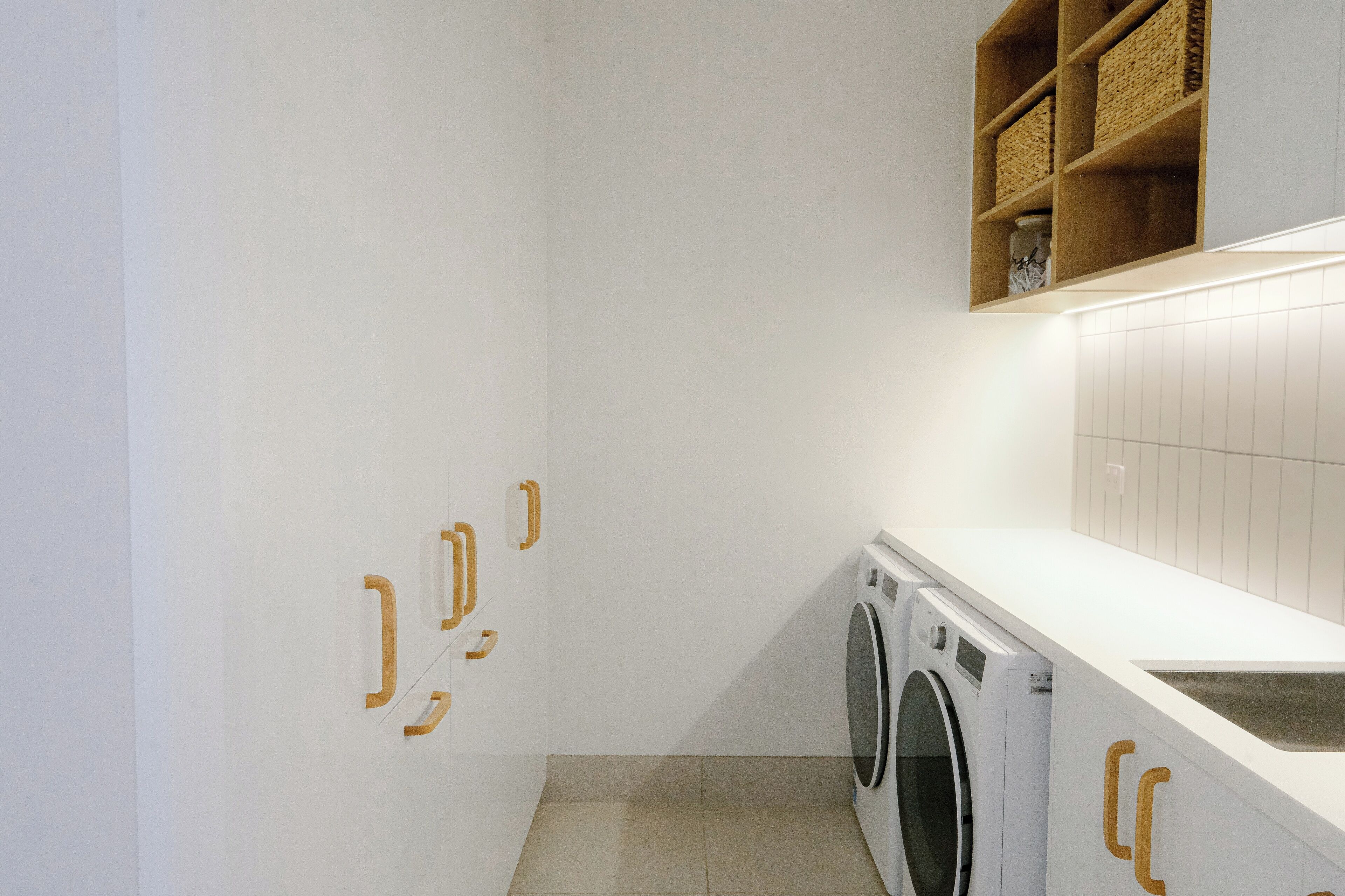 A laundry room with a washing machine, a sink, and wooden shelves above.