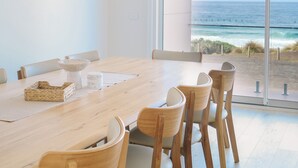 A dining area with a wooden table and chairs, large windows with a view of the ocean. - Oceanview Escape - Luxury New Beachfront Haven w/Hot Tub! (Surf Beach)