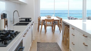 A modern kitchen with a view of the sea, wooden cabinets, and a dining area with a view. - Oceanview Escape - Luxury New Beachfront Haven w/Hot Tub! (Surf Beach)