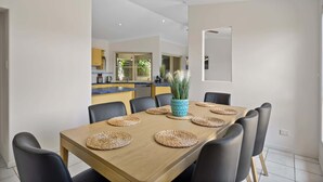 A dining area with a wooden table, black chairs, woven placemats, and a decorative vase. - Spacious 4-Bed Family Retreat with Pool Near Beach (Coolum Beach)