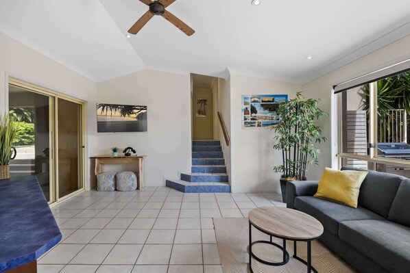 A spacious living area with a staircase, a ceiling fan, a large window, and a sofa with a yellow cushion.