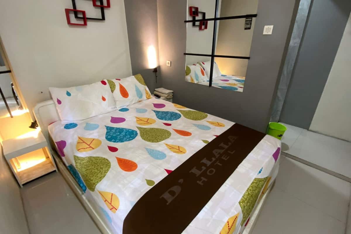 A hotel room with a bed, a nightstand, a mirror, and a green bucket.