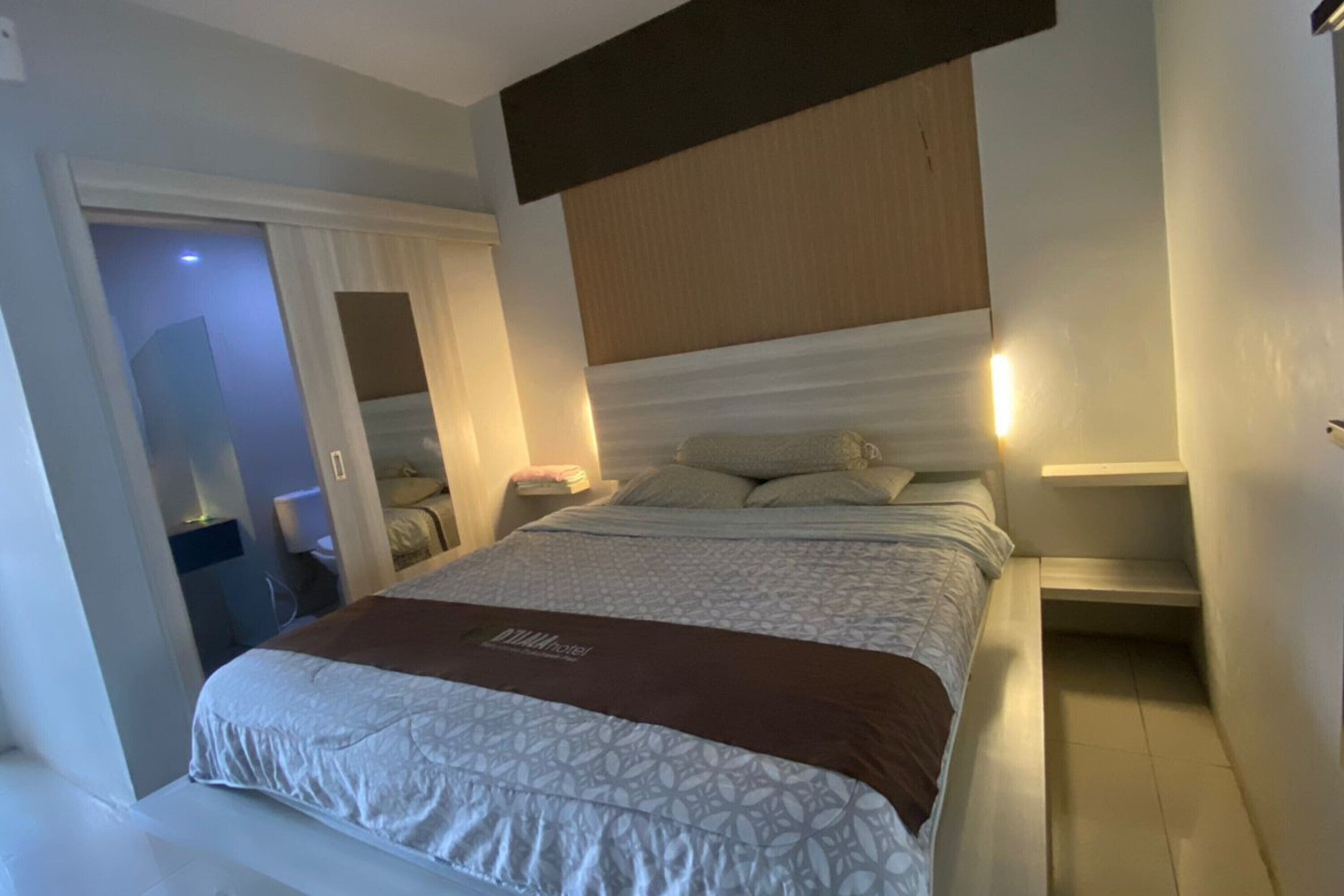 A hotel room with a large bed, a bedside table, a nightstand, a mirror, and a wardrobe.
