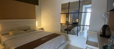 A hotel room with a bed, bedside table, and a mirror.