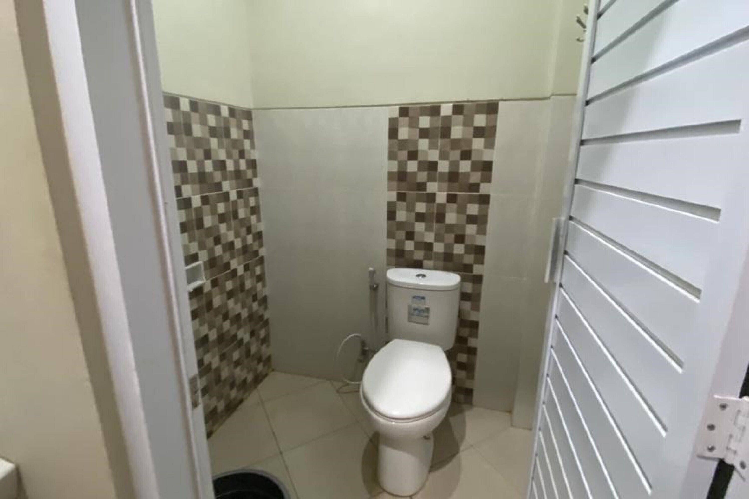 A small, compact bathroom with a toilet, a sink, and a shower. The walls are tiled with a checkered pattern.