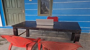 Ein Zimmer mit einem dunklen Holztisch, einem Laptop und zwei roten Plastikstühlen.