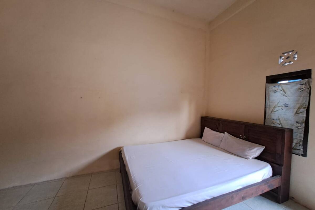 A single bed with a wooden frame and white bedding in a room with plain walls and a tiled floor.