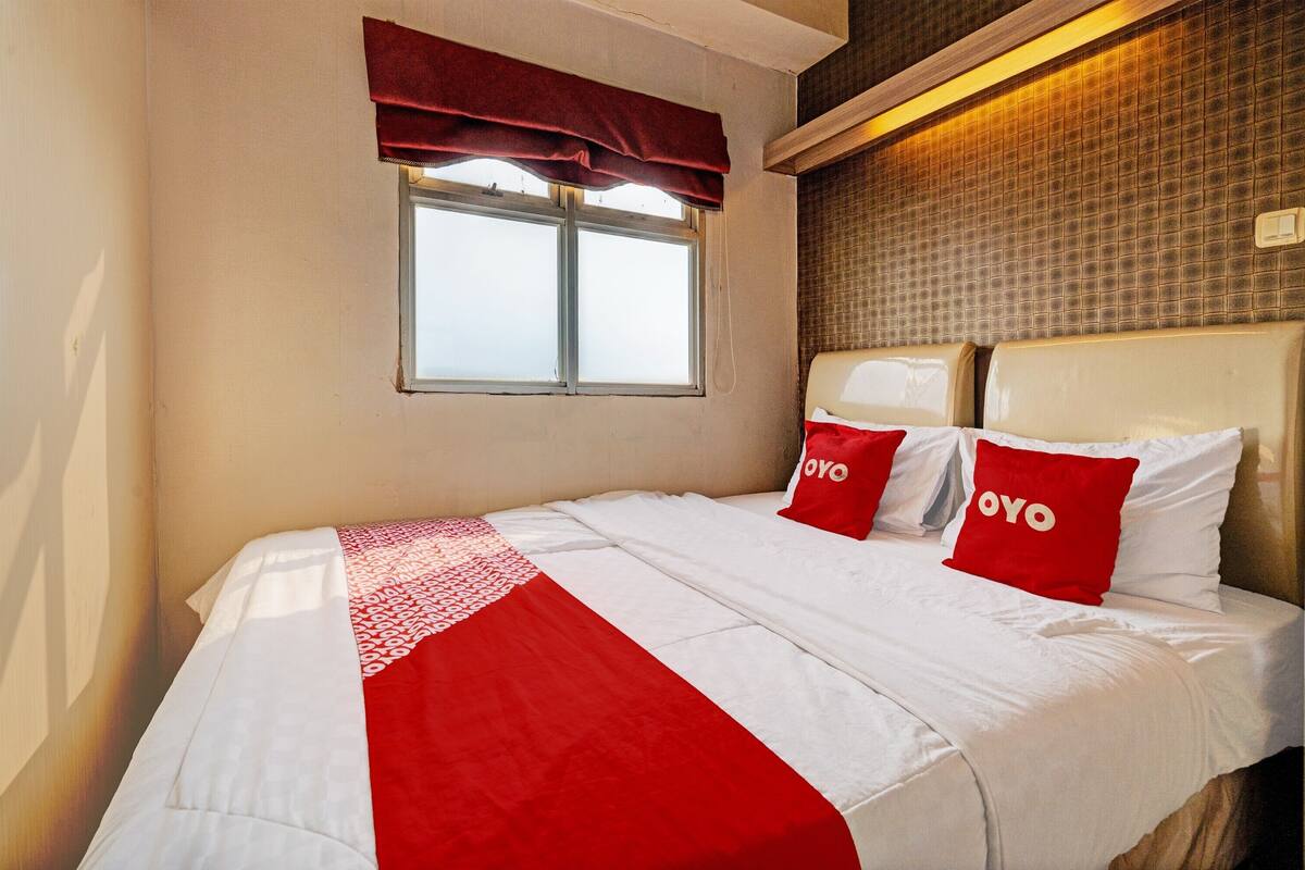 Ein Hotelzimmer mit einem großen Bett, zwei roten Kissen mit der Aufschrift 'OYO' sowie einem Fenster mit roter Vorhangschiene und einer Wand mit Muster.