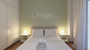Un dormitorio con cama, dos lámparas de noche, una pared con la palabra "Dreams" escrita y una ventana con cortinas.