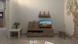 Una sala moderna con un televisor de pantalla plana, mueble de entretenimiento de madera y un mural decorativo con motivos de árboles.