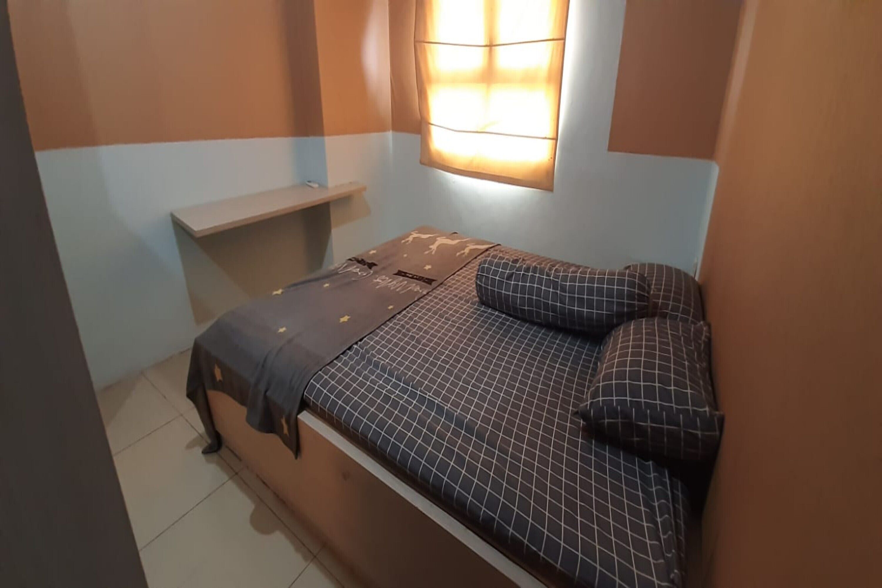 Una habitación pequeña con cama individual, colcha estampada, mesita de noche y ventana con cortinas.