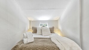 Un dormitorio con cama, almohadas, una colcha y una ventana con luz diurna.