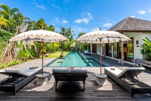 Zona junto a la piscina con sillas de descanso y sombrillas, una terraza de madera y una vista despejada del agua.
