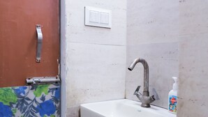 Une salle de bain avec un lavabo blanc, un robinet, un rideau de douche, un distributeur de savon et une porte dotée d’une poignée en métal.