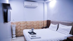Une chambre d’hôtel comprenant un lit, une table de chevet, un climatiseur fixé au mur, un lavabo sur pied blanc et un mur décoré d’un motif en briques.